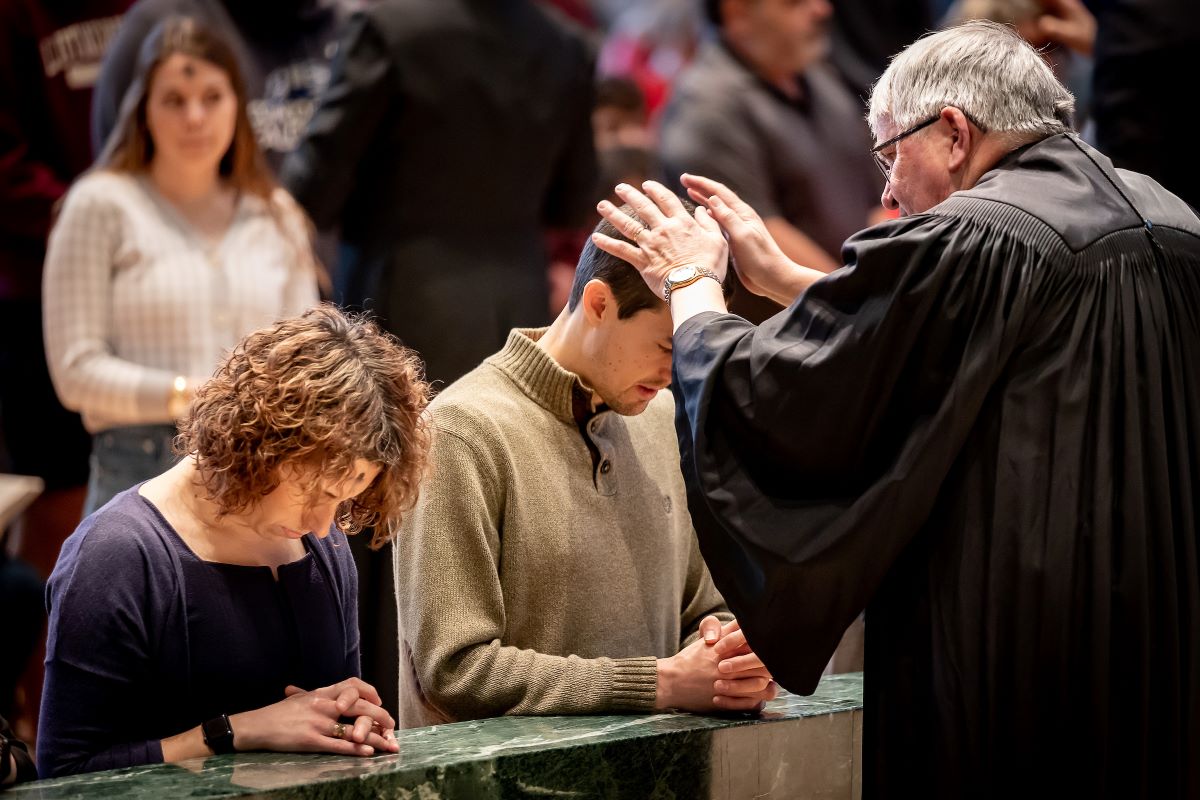 man in black praying over man