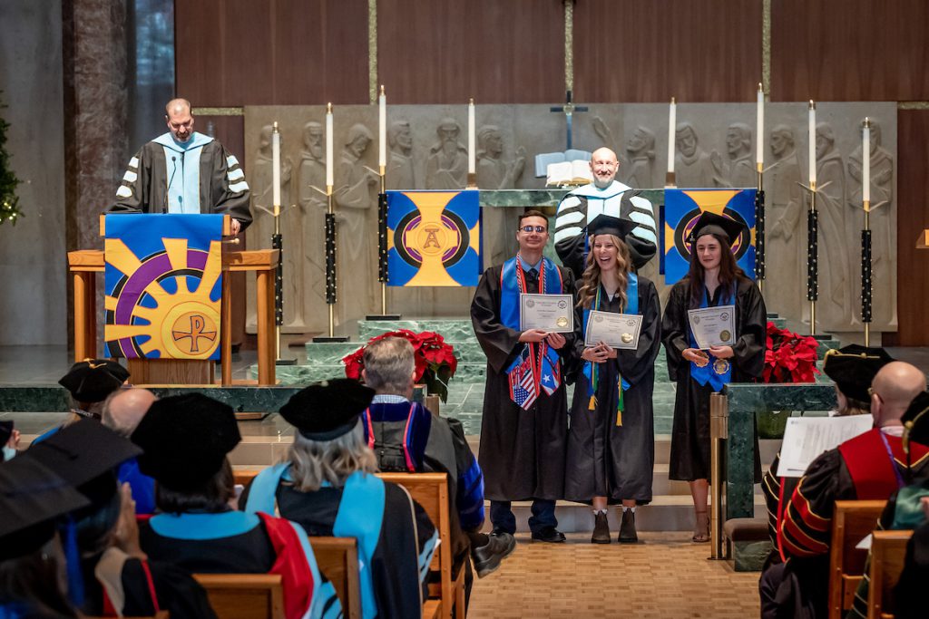 three students receiving degrees in chapel