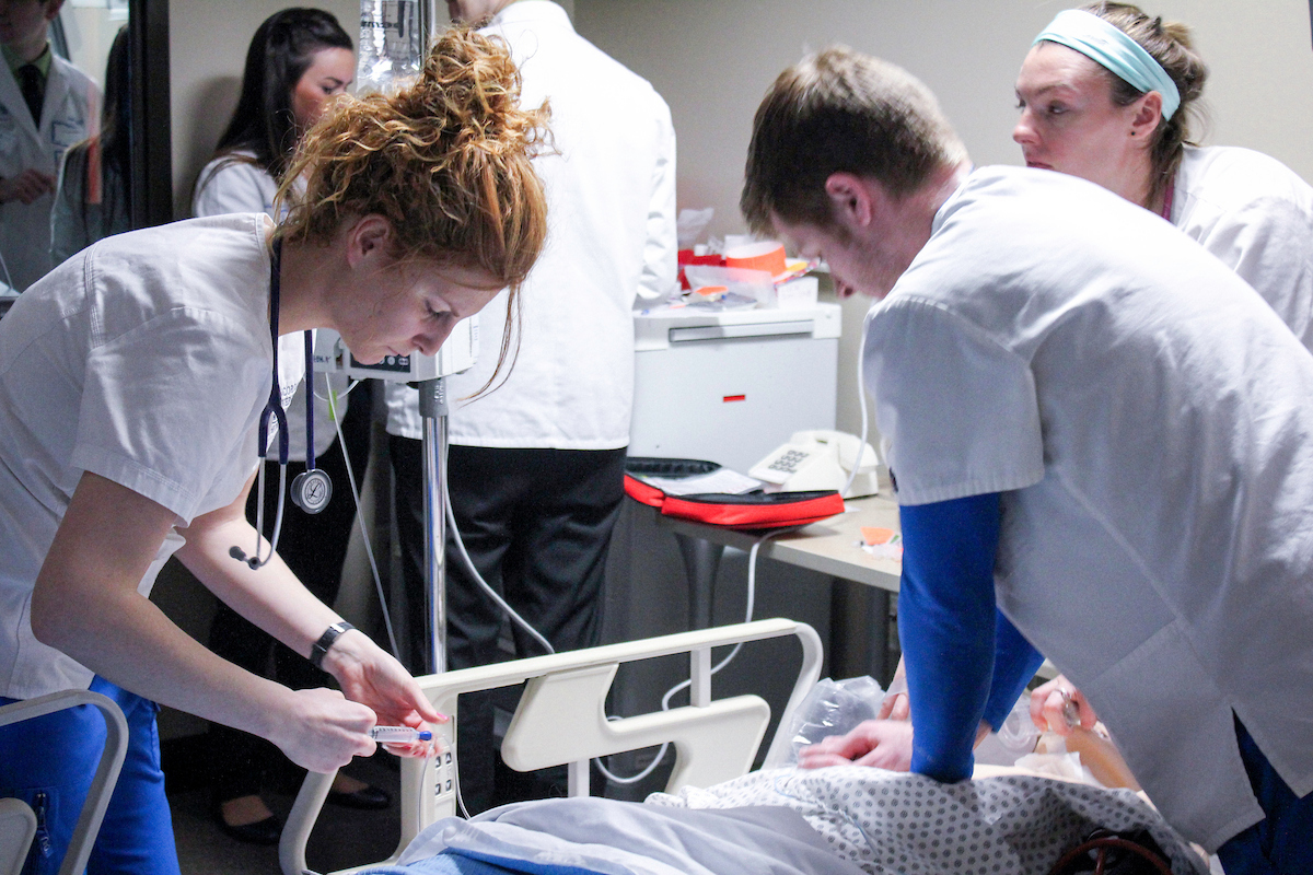 Three students working on "patient" on bed