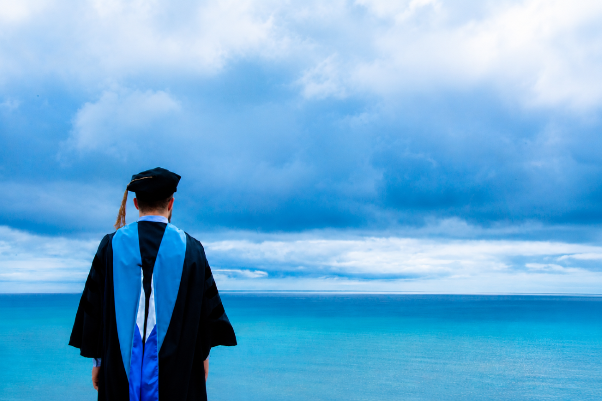 student in robe looking at water
