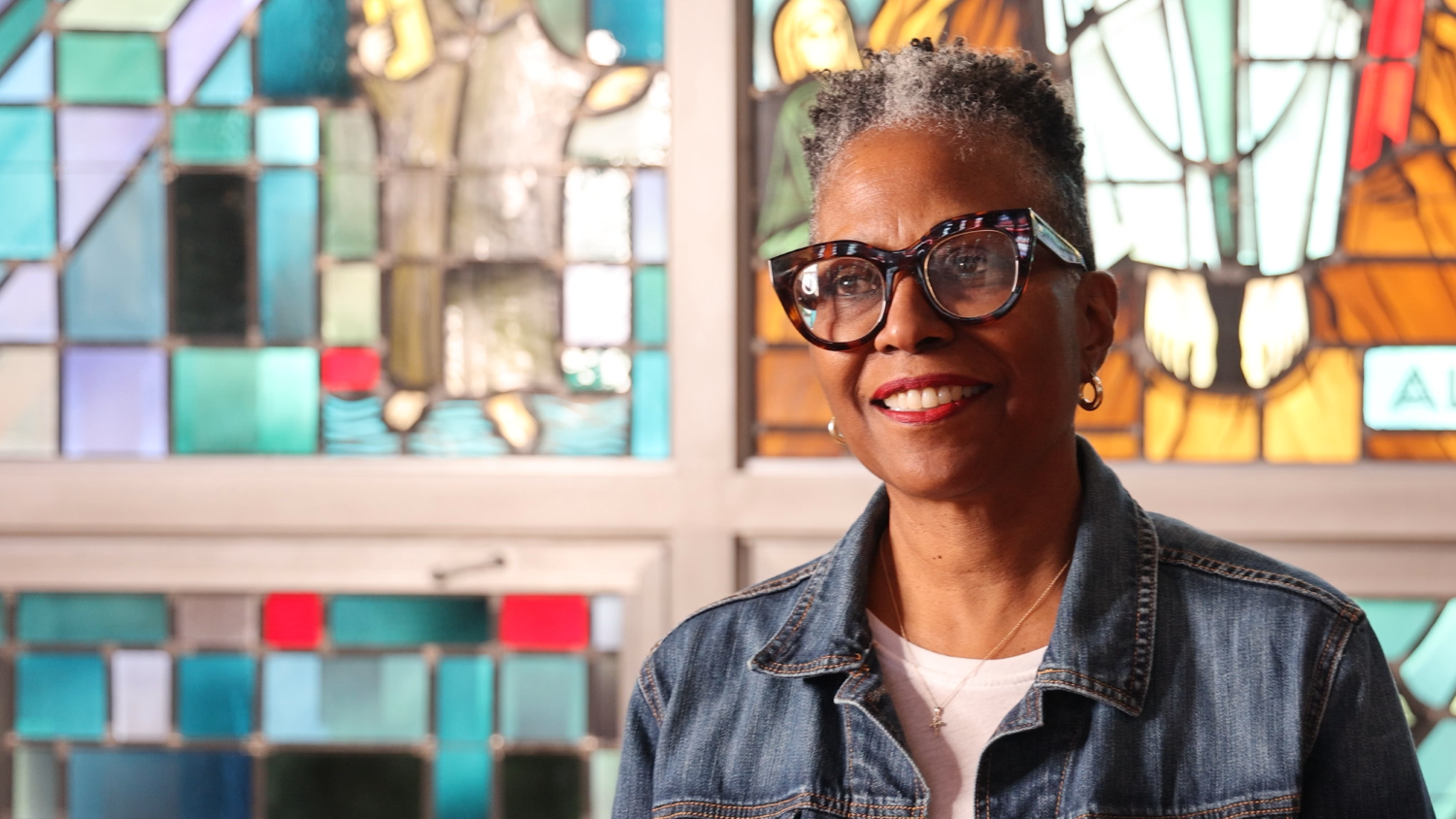 woman with short hair and glasses in front of stained glass window