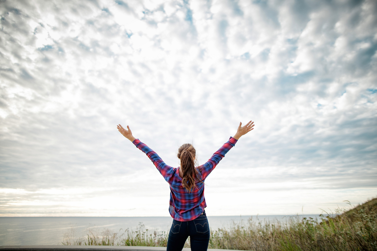 woman with arms raised to sky in front of lake