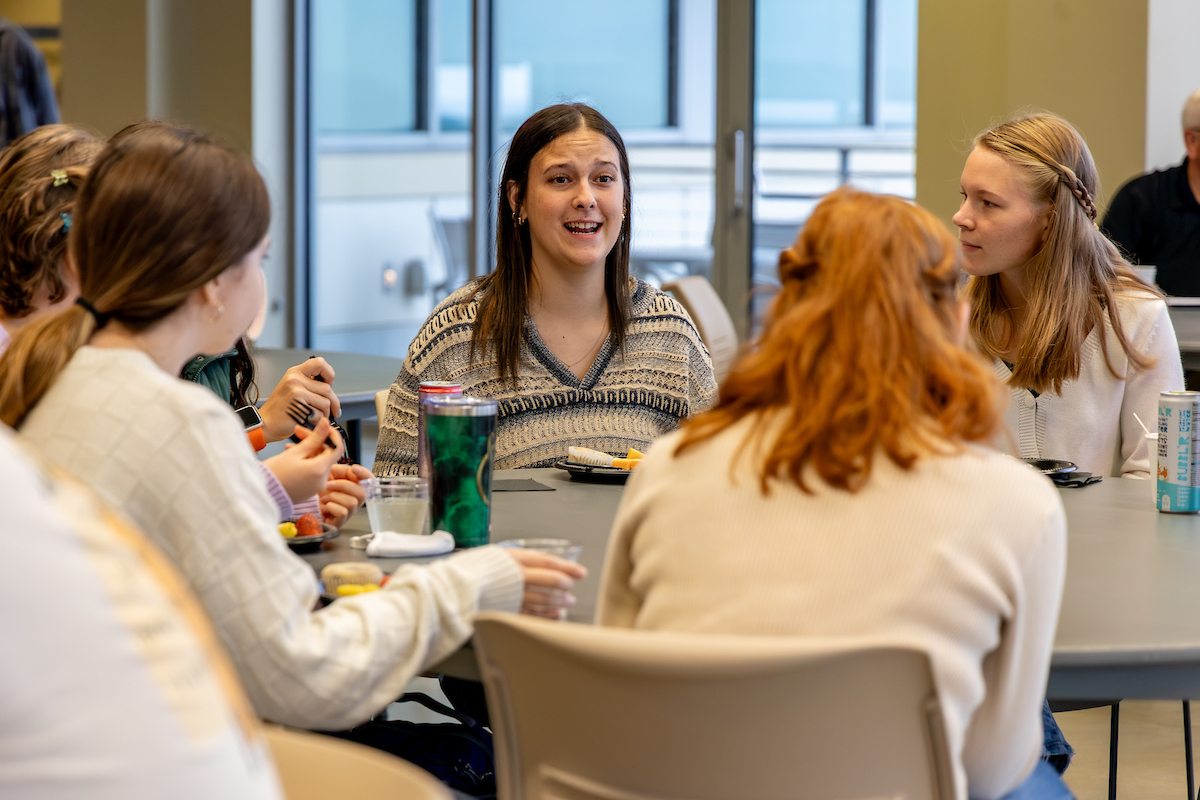 Female student in a striped top seated with other female students at a round table.
