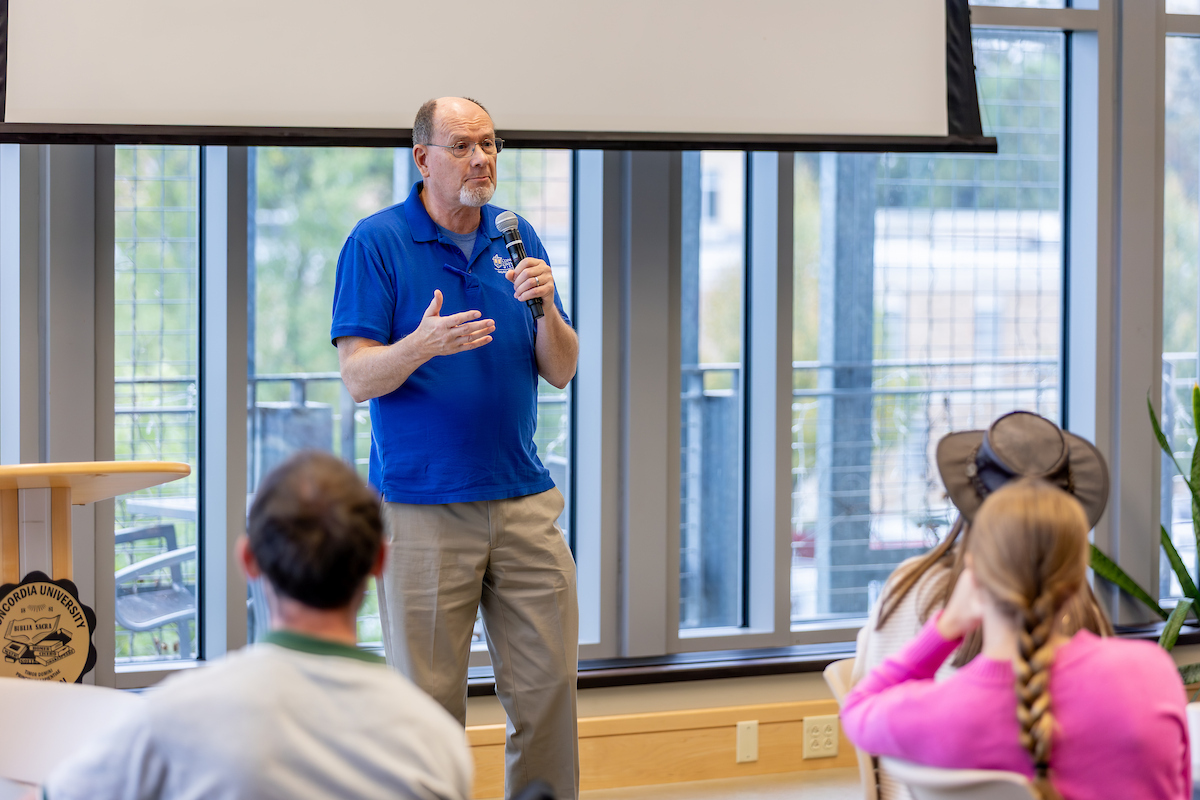 Man in blue shirt talks with a microphone to students 