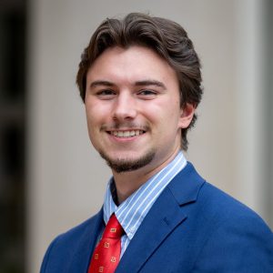 man with brown hair and blue jacket and red tie