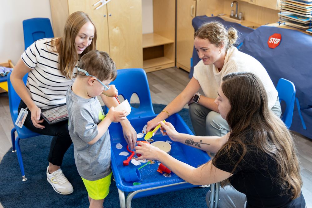 three students working with young boy in sensory bin