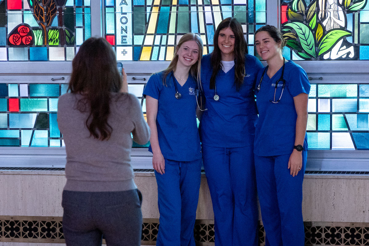 Three nursing students in scrubs posing for a photo in the chapel.