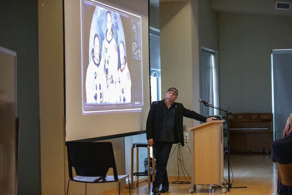 Man leaning on a podium in front of a screen with astronauts on it