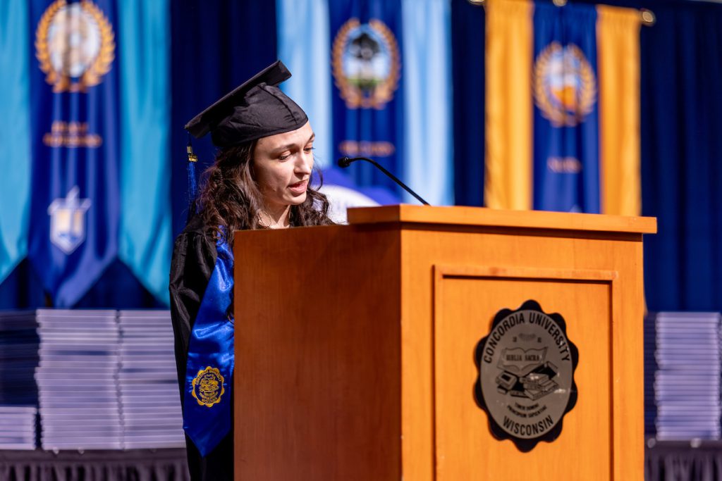 Undergraduate speaker Brianna Lusk delivers remarks at the podium in cap and gown during Concordia’s commencement ceremony.