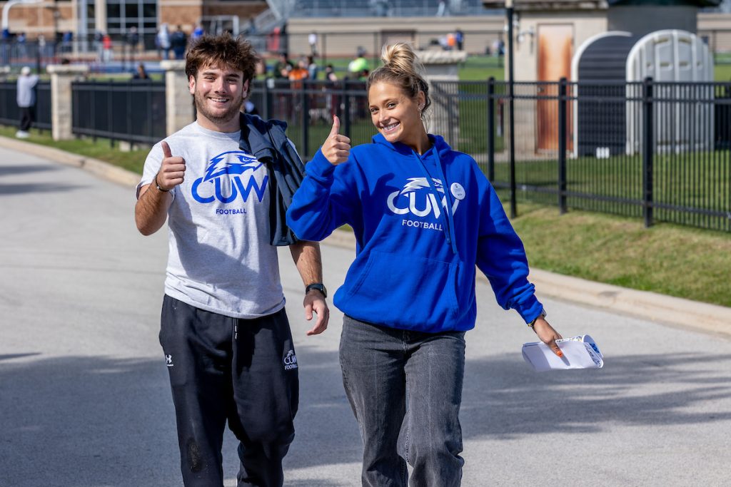 Man and woman student walking on campus together giving the thumbs up.