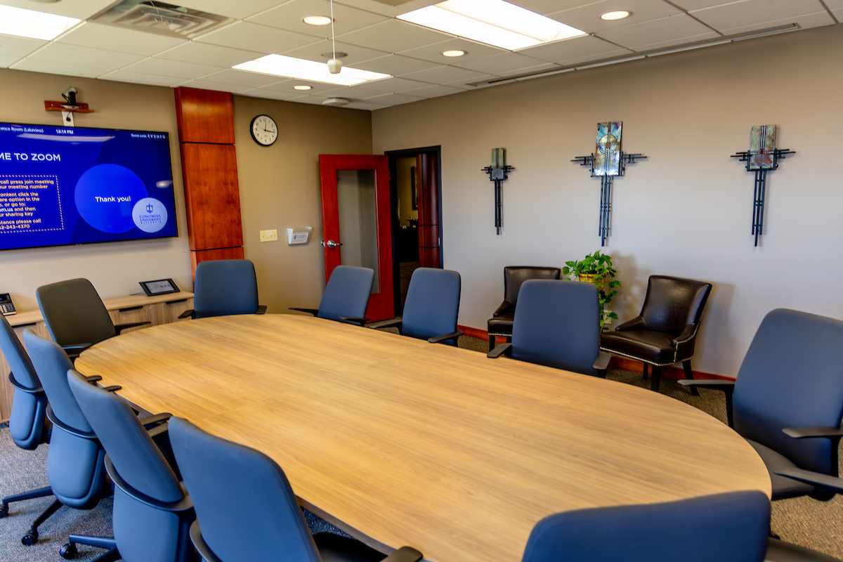large oval table surrounded by blue office chairs with a cross art sculpture on the wall.
