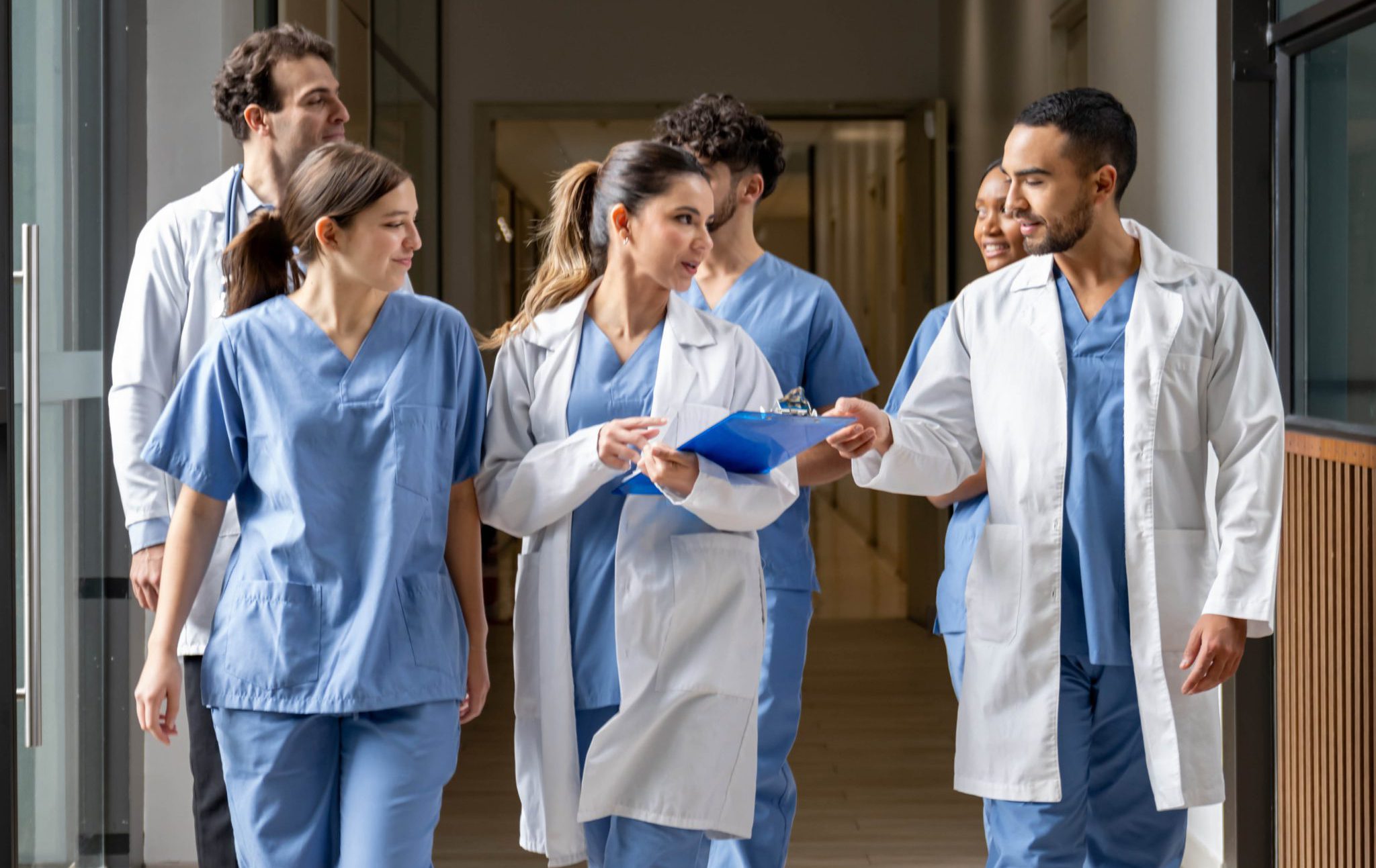 medical students in scrubs and white coats walking the hall together and discussing things