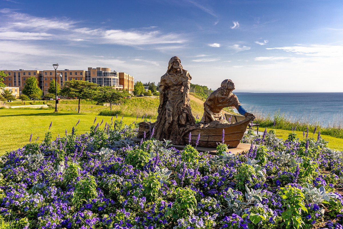 Statue of two men in a boat perched on the bluff, surrounded by flowerrs.