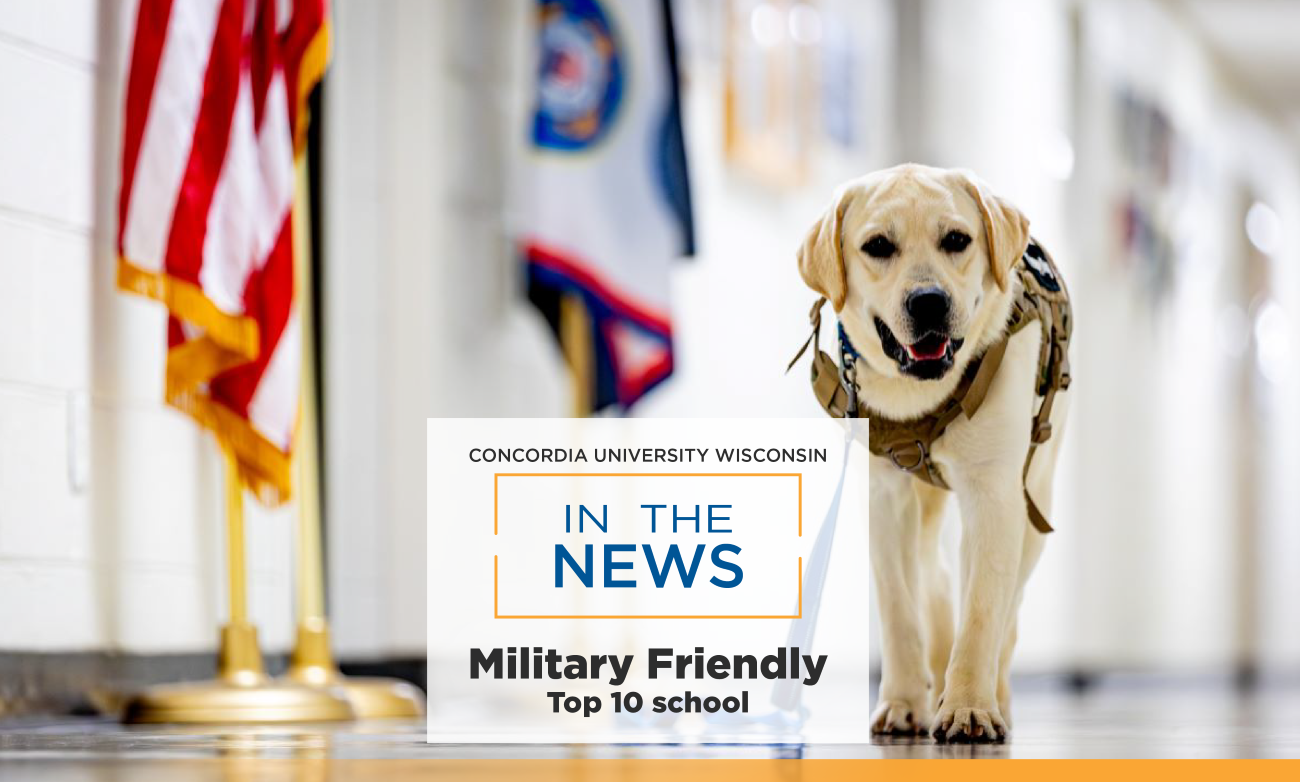 Truman, the veteran resource dog, walks down hall by flags. Words in the news is on top of the photo